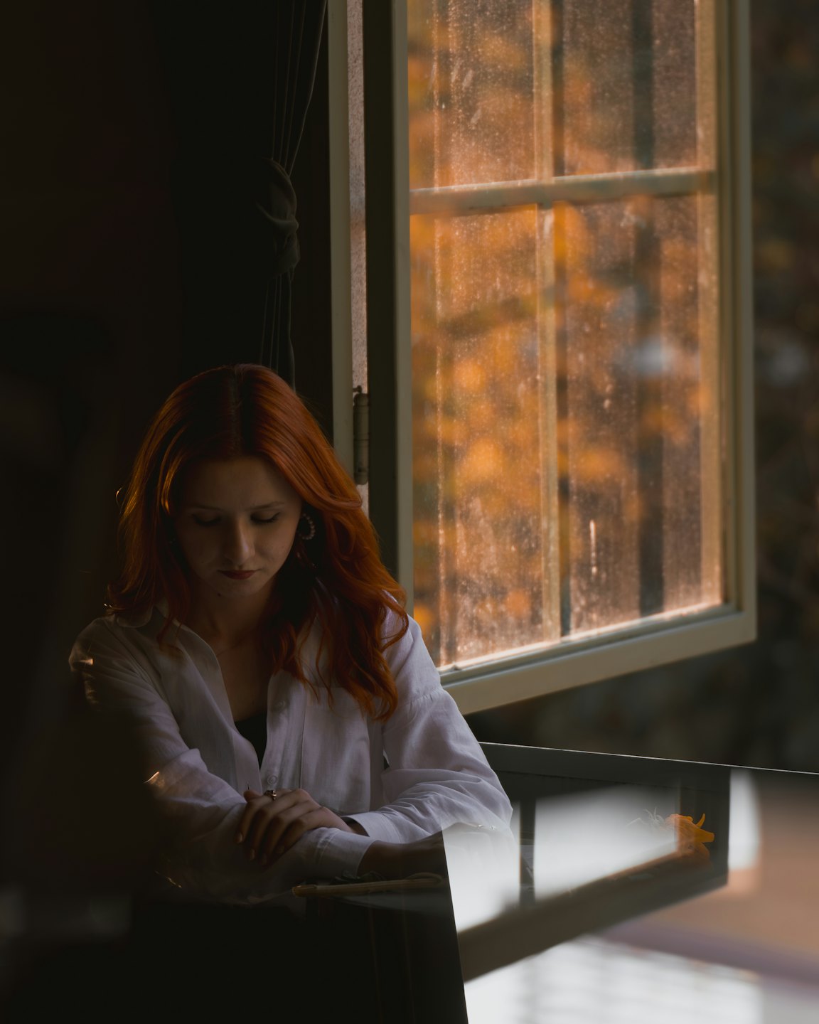 Woman with red hair sits thoughtfully at a reflective table.